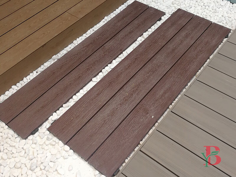 Close-up of dark brown composite decking boards arranged as a garden pathway with decorative white gravel stones.