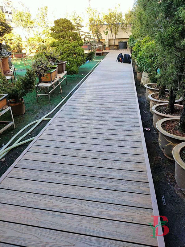 Long grey wood plastic composite (WPC) garden aisle surrounded by potted plants and trees, demonstrating a clean and modern outdoor walkway solution.