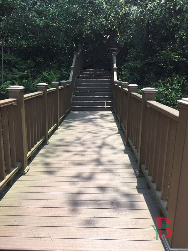 Elevated forest boardwalk made of solid composite decking with traditional railings for nature trails.