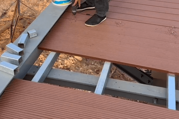 3.metal-fastener-pin-installation-composite-decking Hand inserting a metal fastener pin into a pre-drilled hole on a brown composite deck board