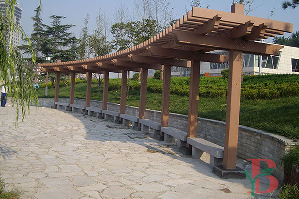 Single-post WPC pergola with one-sided support for unobstructed views along a stone walkway.