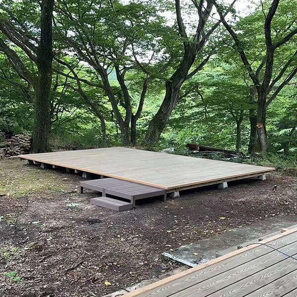 A newly installed standalone rectangular composite deck platform with steps in a wooded forest garden