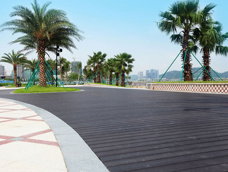 A curved outdoor walkway using walnut capped composite decking boards lined with palm trees