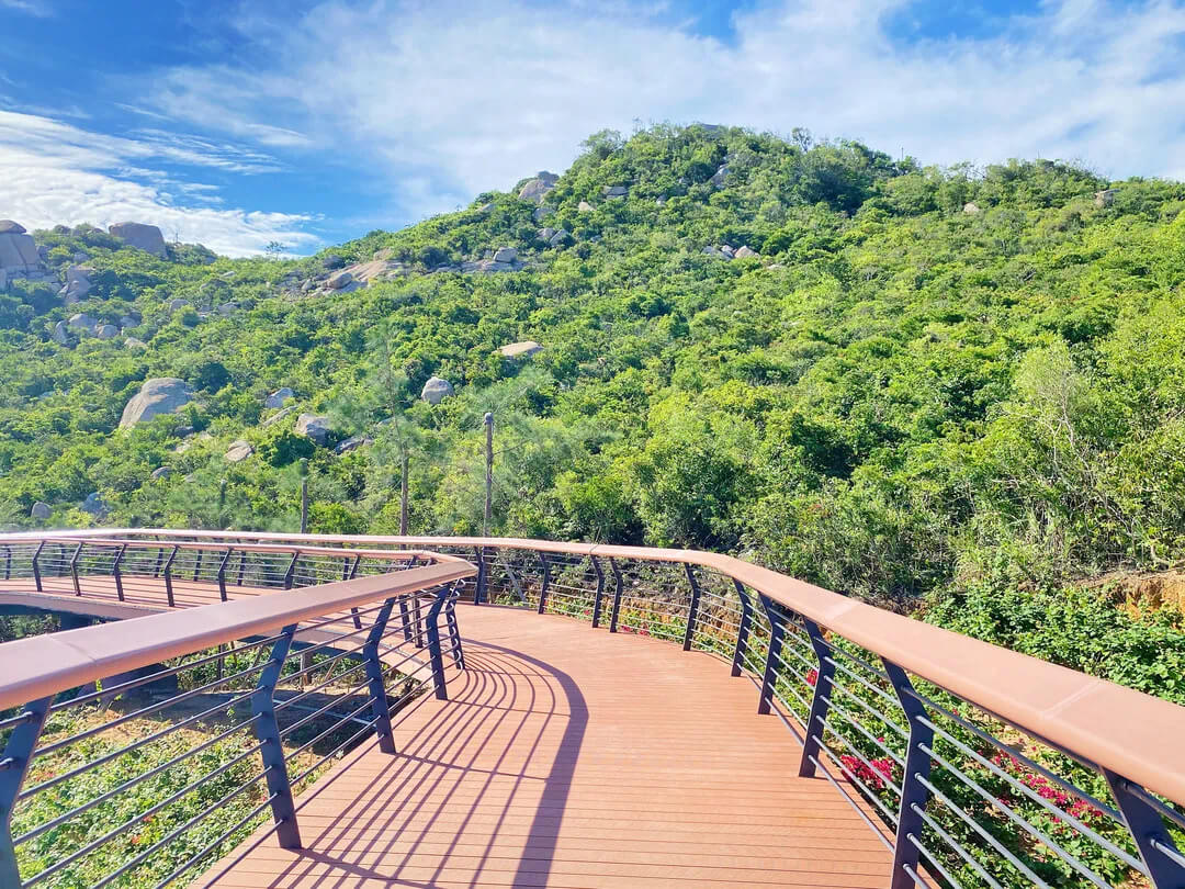 A curved WPC boardwalk with black railings in a scenic mountain park.